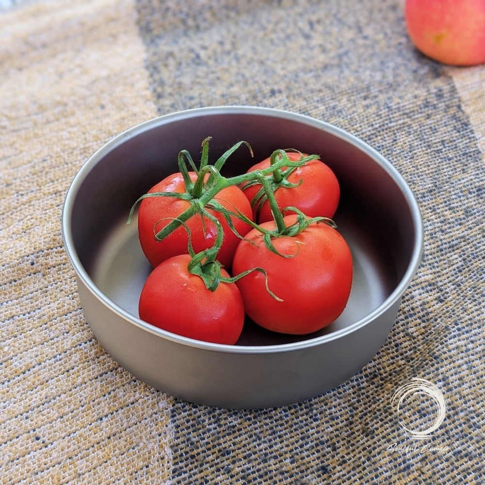 Titanium camping bowl filled with fresh tomatoes on rustic picnic setup