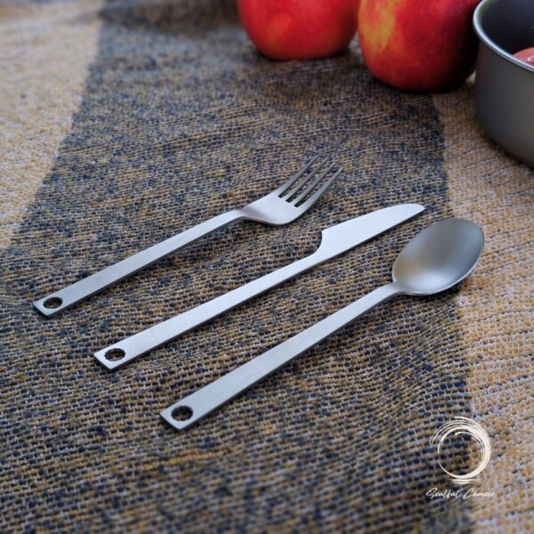 Titanium cutlery set flat lay on rustic camping mat with apples