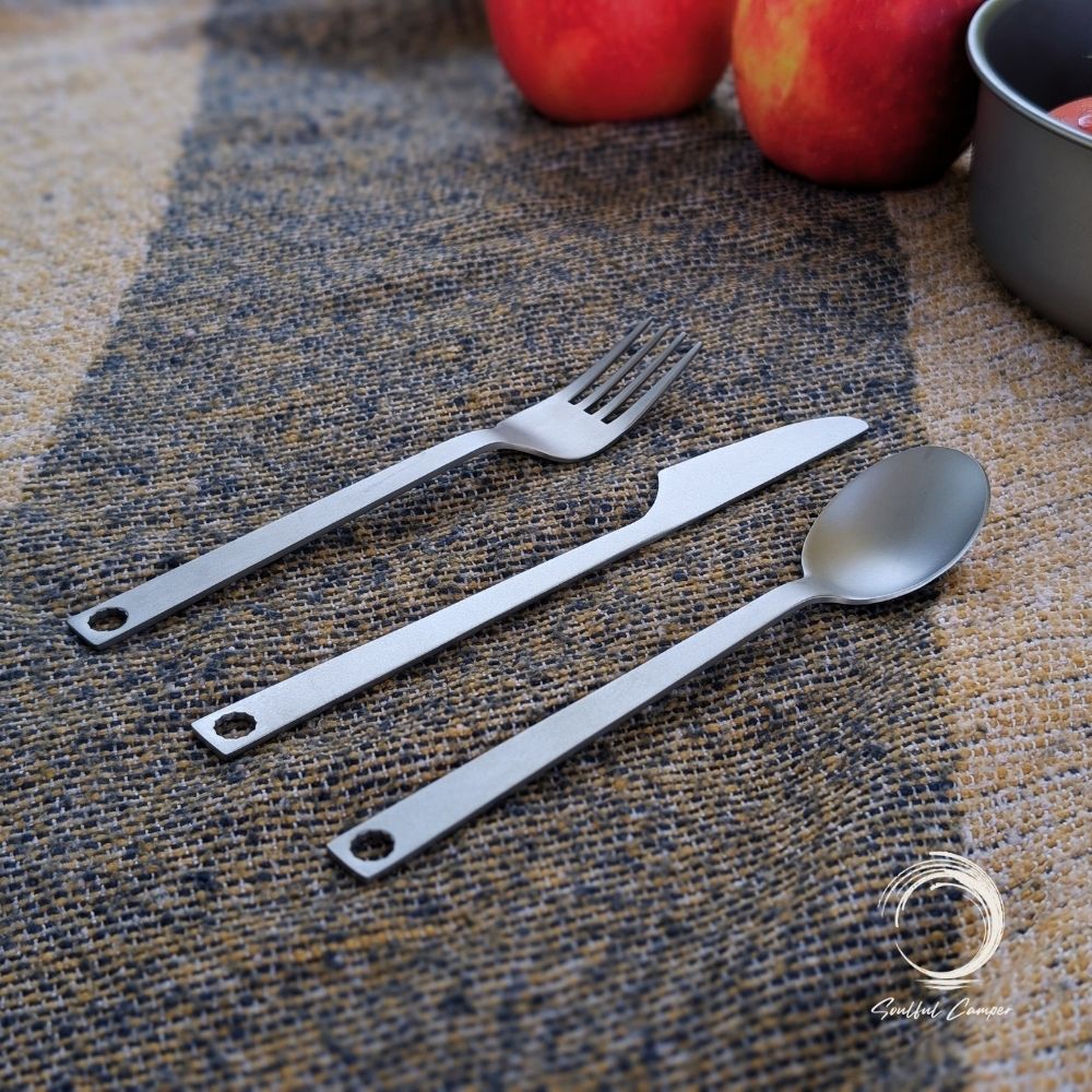 Titanium cutlery set flat lay on rustic camping mat with apples