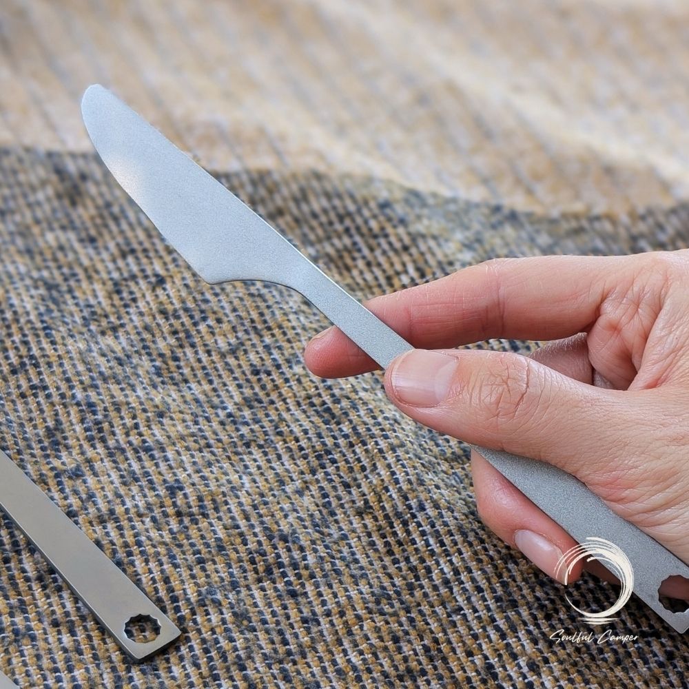 Titanium camping knife held in hand on rustic surface