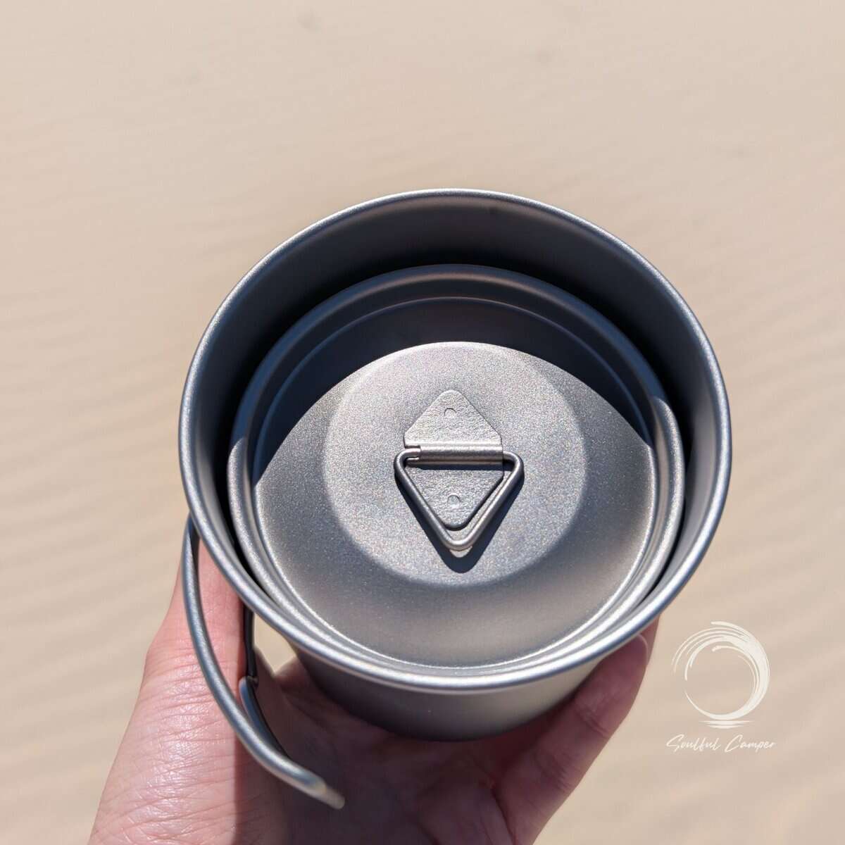 Hand holding the fully nested Ti-3 Mug Stack with lid, showing compact titanium camping mug set for lightweight travel.