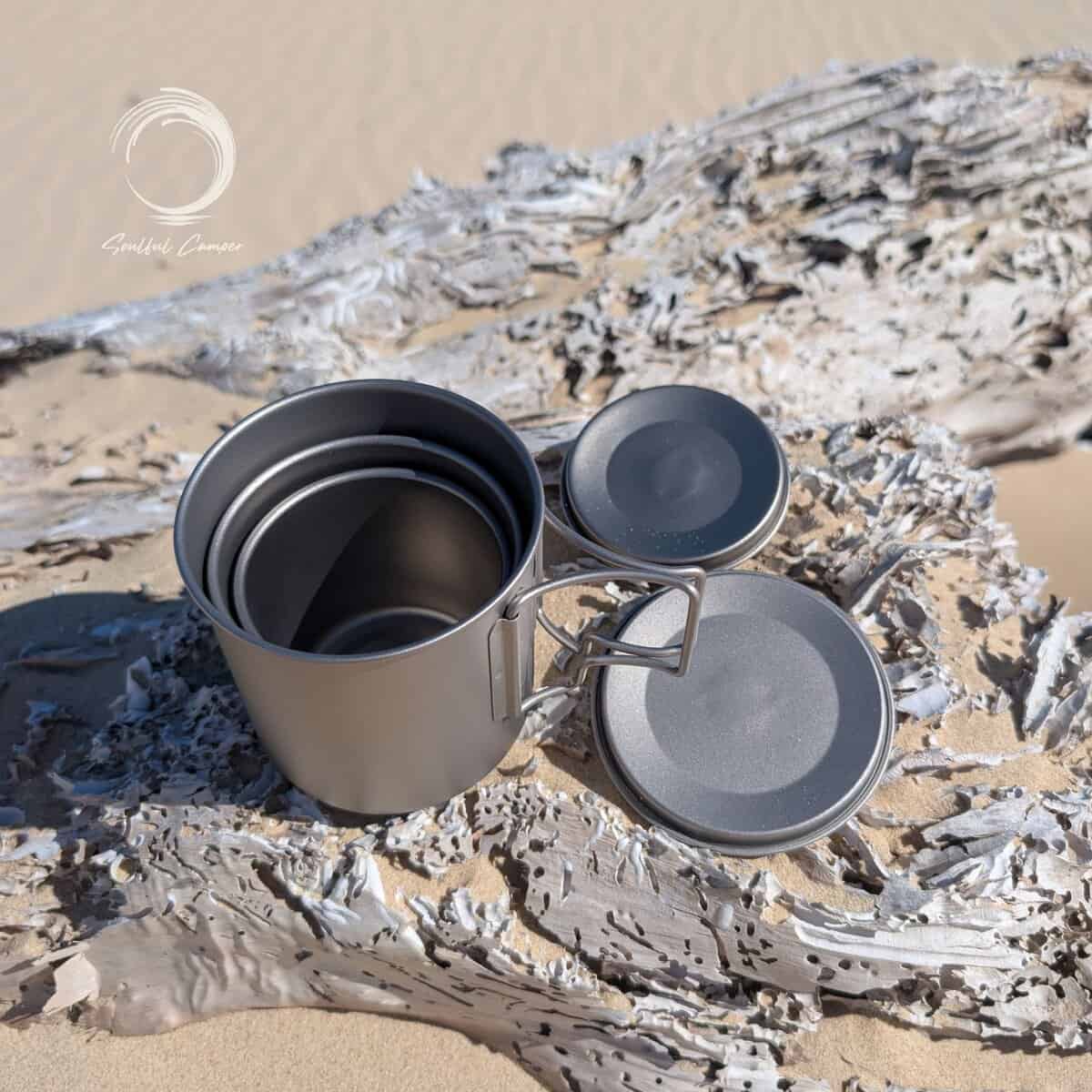 Top-down view of the Ti-3 Mug Stack showing three titanium mugs neatly nested together with matching lids on driftwood.